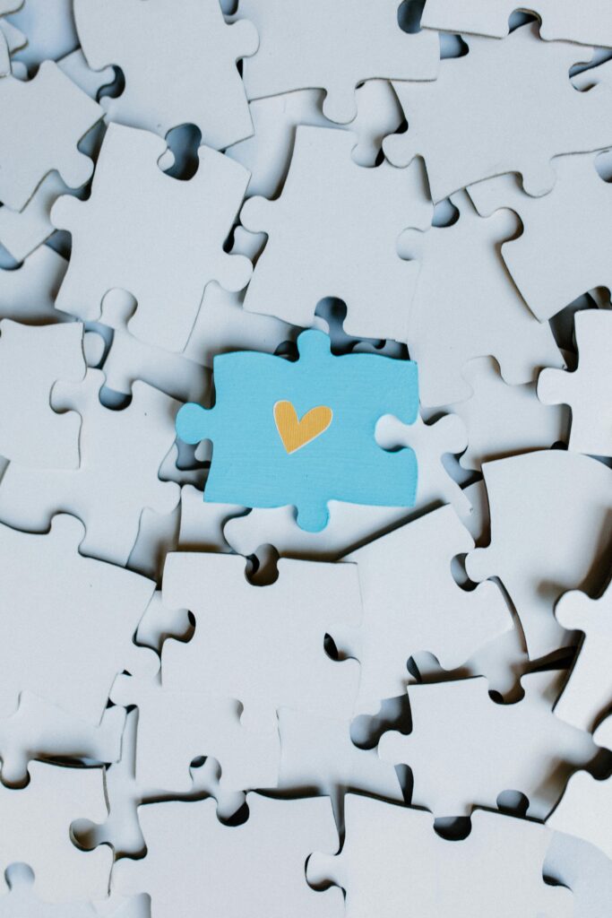 A single blue puzzle piece with a heart stands out in a sea of white pieces.