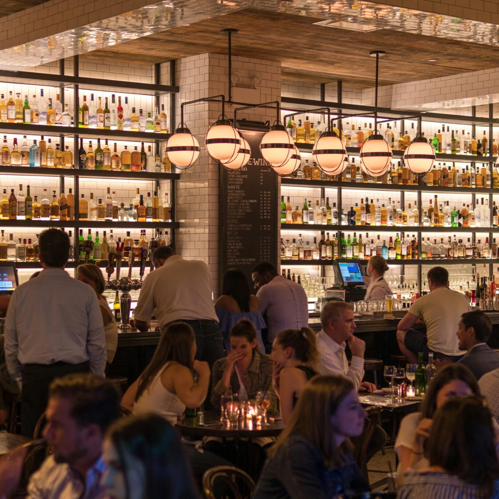Experience the lively atmosphere of a bustling New York City bar with patrons enjoying nightlife within a stylish indoor setting.