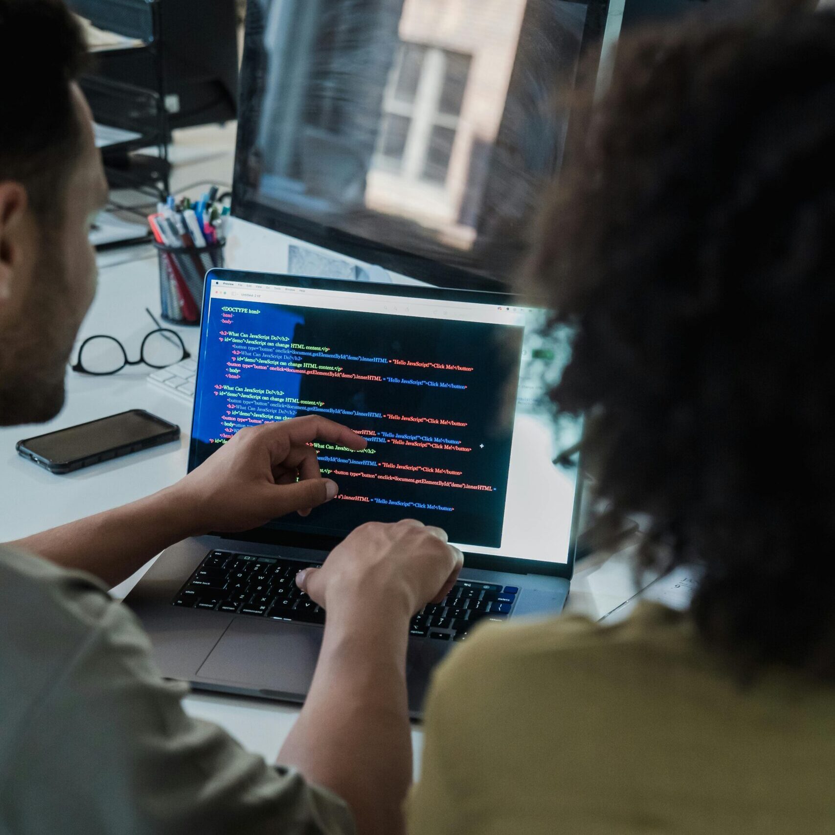 Two adults collaborating on programming tasks using a laptop in an office setting.