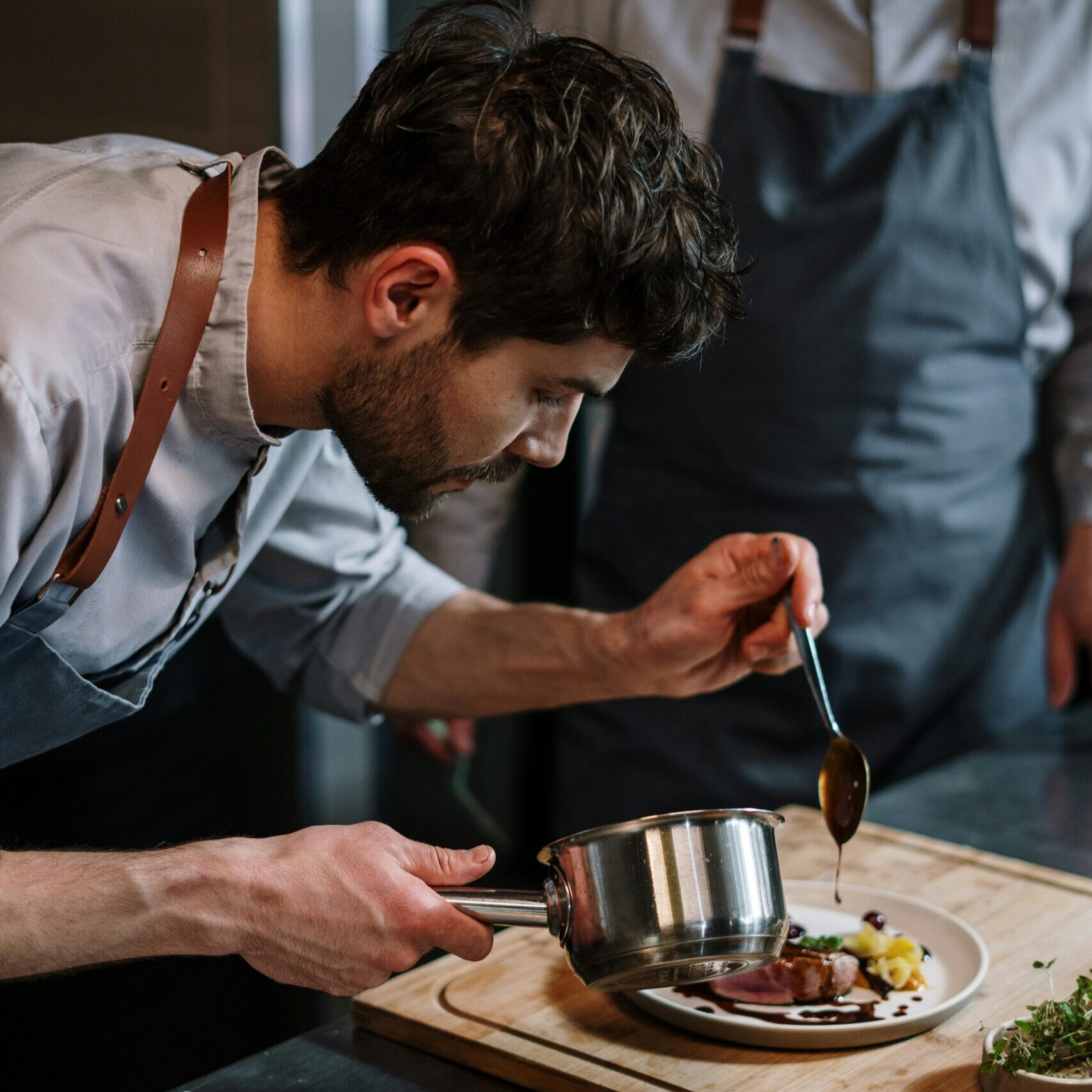 Two chefs in aprons skillfully plating a gourmet dish in an industrial kitchen setting.