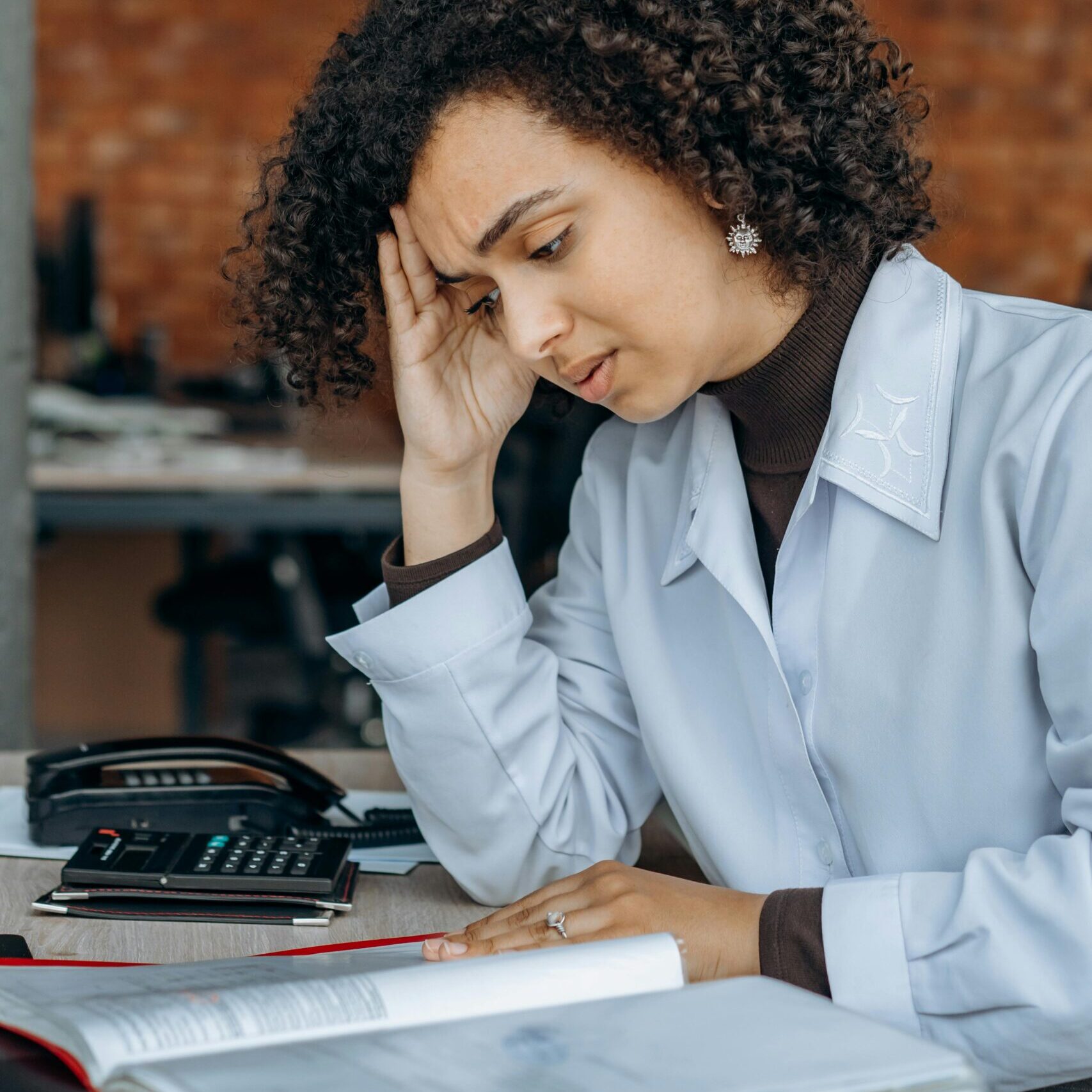 Exhausted woman in office with paperwork, displaying signs of stress.