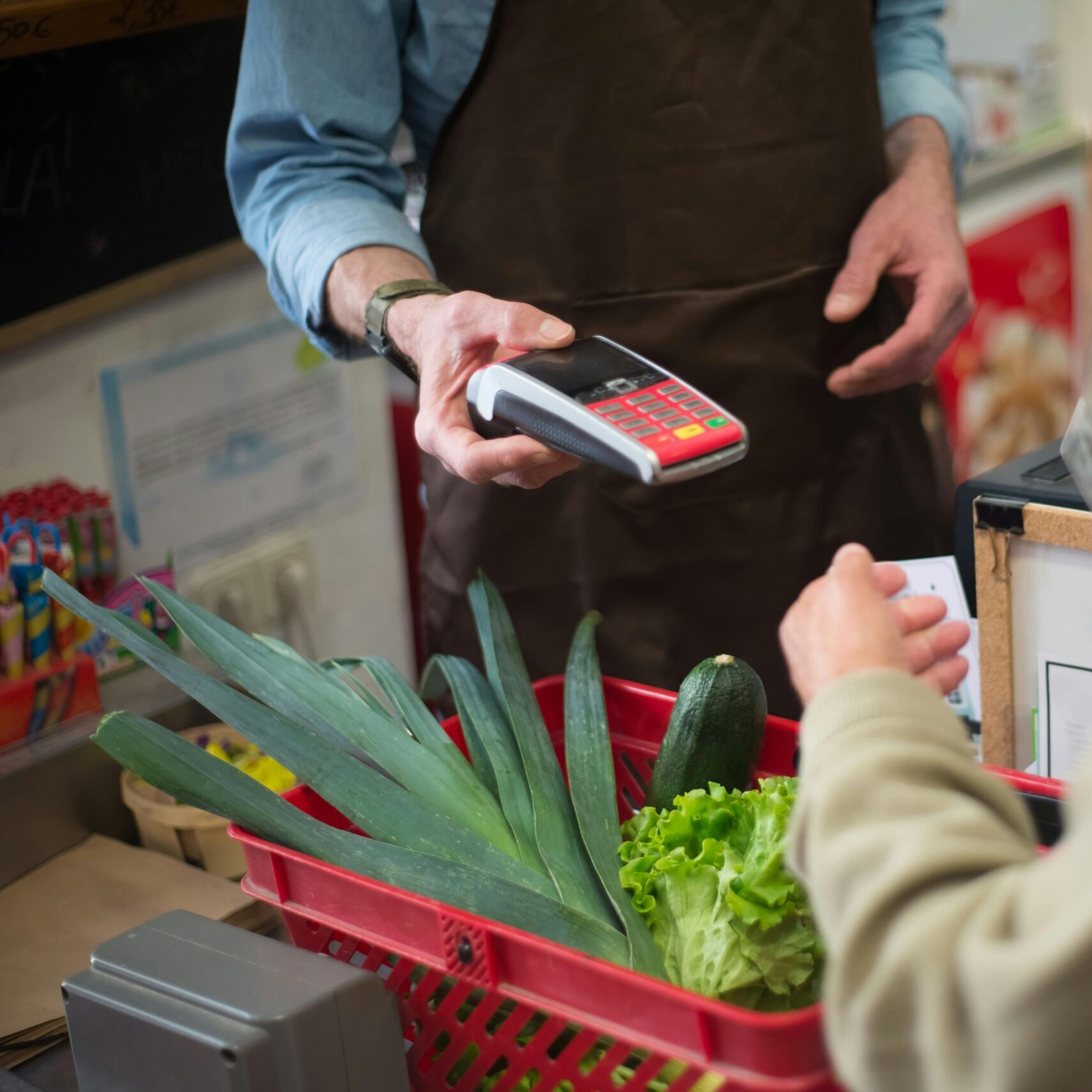 Close-up of customer paying for groceries with produce at a store checkout counter.