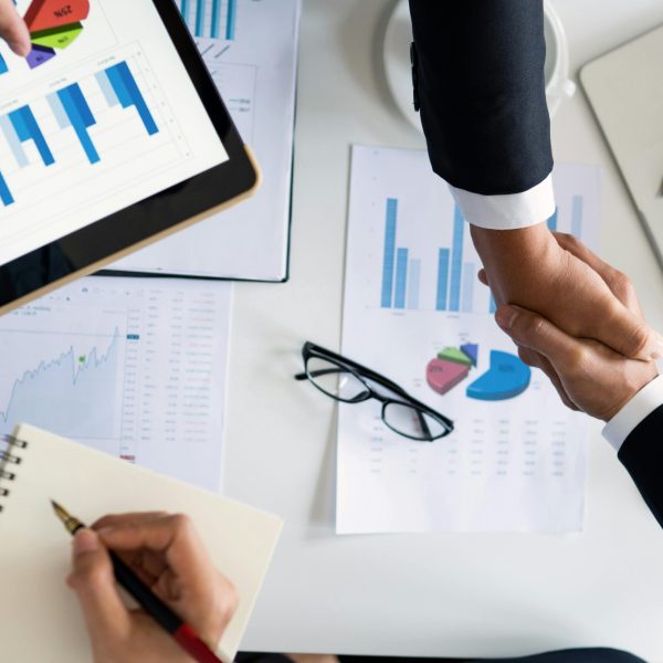 Business professionals handshake over graphs and charts in a corporate setting, symbolizing successful negotiation and agreement.