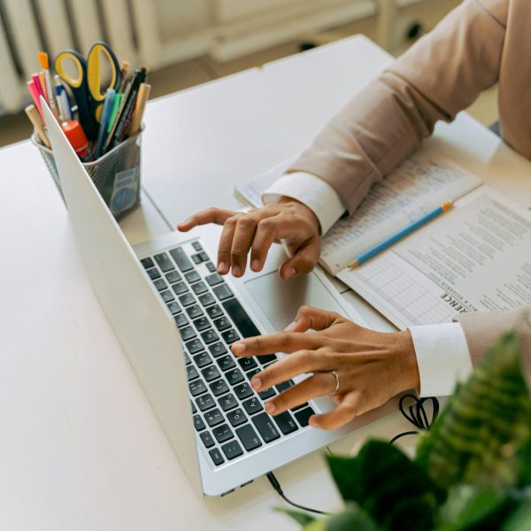 A business professional typing on a laptop at a well-organized office desk with plants and stationery.