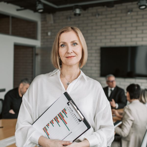 Professional woman holding clipboard in corporate office setting during a business meeting.