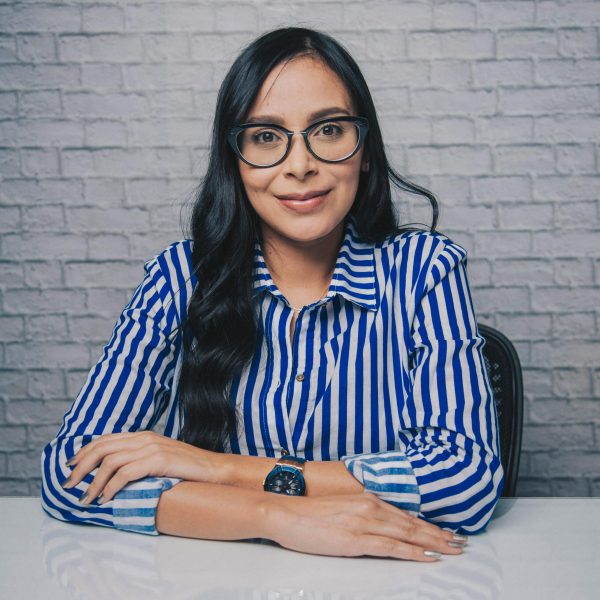 Young female in striped t shirt and eyeglasses sitting near at table white brick wall with crossed arms