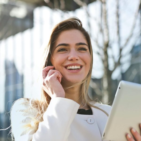 Confident businesswoman using her tablet and phone, smiling outdoors in sunlight.