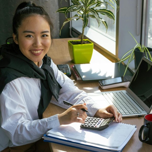 Confident woman working with calculator in bright office setting, surrounded by office tools.